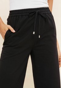 Czarne dresy z elastycznym pasem i sznurkiem do regulacji, kieszeniami bocznymi oraz gładką teksturą z mieszanki bawełny.