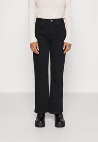 Svart denim med utsvängda ben, hög midja och fem fickor, parat med en krämfärgad ribbad långärmad topp och kraftiga svarta stövlar.