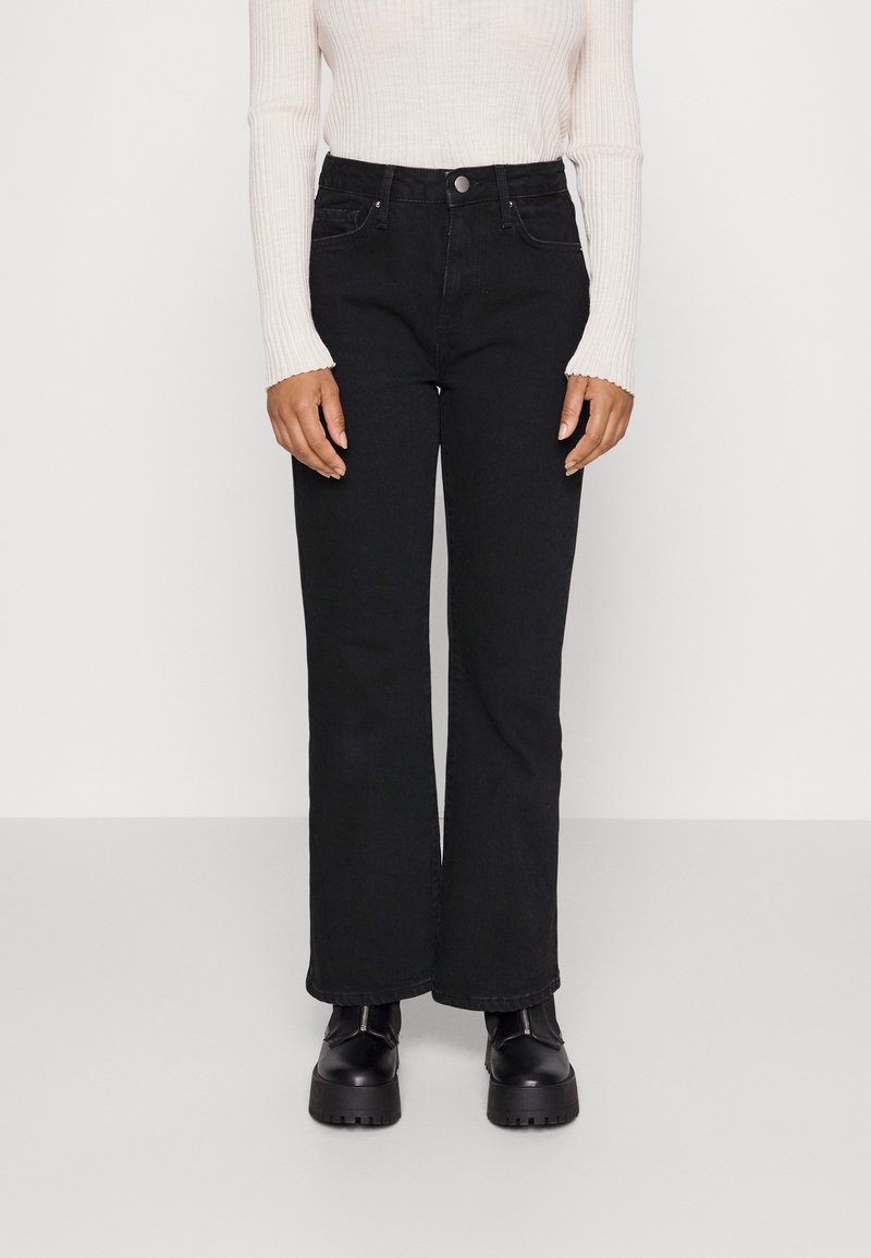 Svart denim med utsvängda ben, hög midja och fem fickor, parat med en krämfärgad ribbad långärmad topp och kraftiga svarta stövlar.