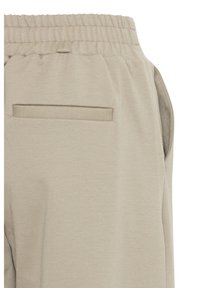 Gros plan sur un pantalon beige avec une taille élastique et une unique poche arrière horizontale côté droit.