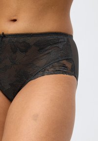 Črni hlačke iz čipke z visokim pasom, cvetličnim vzorcem in valovitim robovima, z gladkim, trdnim črnim zadnjim delom in mehko teksturo.