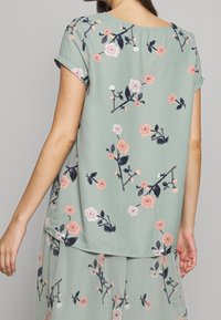 Grön blommig blus med korta ärmar, tillverkad av ett lätt material, med rosa och vita blommönster samt rund halsringning.