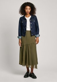 Veste en denim bleu foncé, t-shirt blanc, jupe à volants verte olive, et chaussures à plateforme noires avec des accents cloutés.