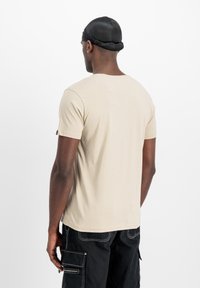 Beige T-Shirt mit kurzen Ärmeln und glatter Textur, Rundhalsausschnitt und taillierter Passform, kombiniert mit schwarzen Cargo-Hosen und einem schwarzen Durag.