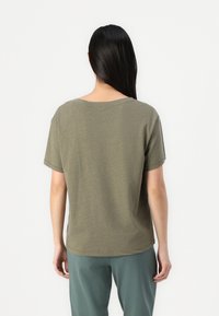 Olive green cotton t-shirt with short sleeves, relaxed fit, wide neckline, and a smooth texture, paired with loose green pants.