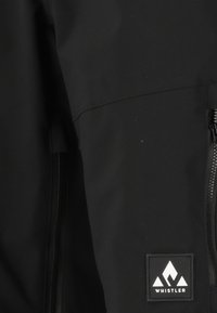 Zwarte, waterproof jas met een gladde textuur, voorzien van een rits aan de voorkant en een klein wit logo-label met de tekst "WHISTLER."