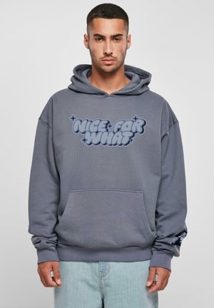 Grå oversized hettegenser med en stor blå grafisk tekst "NICE FOR WHAT" på forsiden, kengurulomme og ribbestrikkede ermer.