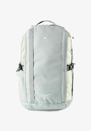 Mochila compacta de color gris claro con correa vertical en la parte delantera, hebillas laterales, asa en la parte superior y texto "TIGHT Junior 15" en el panel frontal.