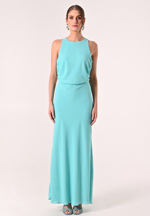 Robe maxi aqua en tissu léger avec un design sans manches et un détail de taille froncée. Portée avec des sandales à talons aqua assorties.