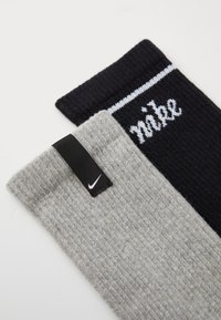 Kaks sokki: üks hall, tekstureeritud kudum musta sildiga ja teine must valgete horisontaalsete triipudega ning valge õmblusega "nike" logo.