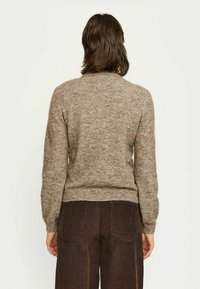 Rjav pleten pulover z teksturirano površino, oprijetimi rokavi in krožnim izrezom, v kombinaciji s temnimi kordurojskimi hlačami.