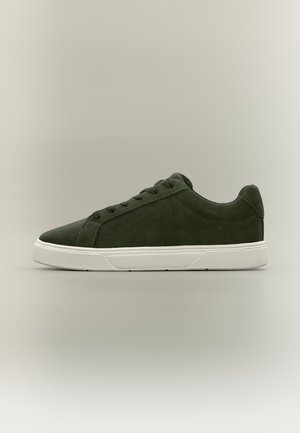 Donkergroene suède lage sneaker met bijpassende veters en witte rubberen zool, getoond vanaf de rechterkant op een neutrale achtergrond.