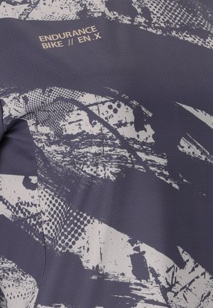 Nahaufnahme eines dunklen Stoffs mit abstraktem weißem Farbspritzmuster und dem Text "ENDURANCE BIKE // EN.X" nahe der Oberkante gedruckt.