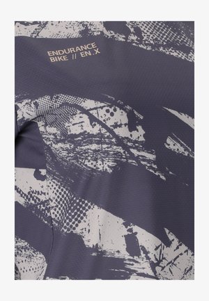 Nahaufnahme eines dunklen Stoffs mit abstraktem weißem Farbspritzmuster und dem Text "ENDURANCE BIKE // EN.X" nahe der Oberkante gedruckt.
