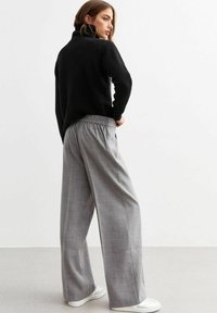 Zwarte, hoog gesloten trui gecombineerd met losse, grijs geblokte broek. Het ontwerp heeft een elastische tailleband en casual witte schoenen.