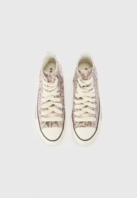 Höga sneakers med krämfärgade snören och sulor, med ett mönster av rosa och svart ormskinn, uppställda sida vid sida mot en vit bakgrund.