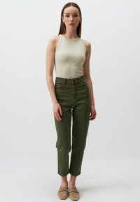 Rippentop in Beige, kombiniert mit hoch taillierten, olivgrünen, schmal zulaufenden Jeans mit seitlichen Taschen und weichen, beigen Slippers.