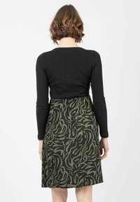 Schwarz geripptes Langarmoberteil, das zu einemRock mit grünem und schwarzem Muster in abstraktem Design übergeht, wodurch eine taillierte und ausgestellte Silhouette entsteht.