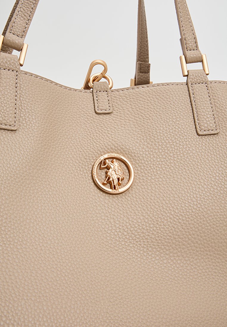 Sac en cuir texturé beige avec poignées doubles et un emblème rond en ton doré représentant un cavalier.