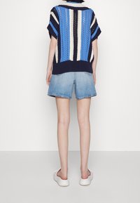 Pull en tricot avec des rayures bleues, crème et bleu marine ; manches courtes et coupe ample. Assorti à un short en denim bleu clair et des chaussures blanches.