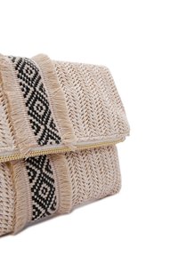 Bolso de mano tejido en color beige con bordes deshilachados, que presenta una franja de patrón geométrico negro y una cremallera de metal dorado. Detalle de superficie texturizada destacado.