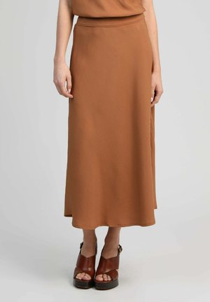 Femme portant une jupe marron taille haute, longueur cheville, associée à des sandales à plateforme marron avec des brides à la cheville.