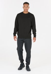 Svart sweatshirt med ribbade muddar och nederkant, i kombination med mörka joggers. Enkelt design, tillverkad av bomullsblandat material, med minimal logotyp.