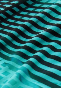 Tela tejida con rayas turquesa y negras, de textura suave. El patrón incluye diseños alternados de ondas y líneas.