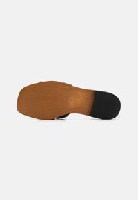 Sole in legno marrone con tacco in gomma nera testurizzata; design della fascetta superiore liscia in nero. Superficie antiscivolo con profilo piatto.