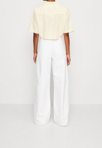 Chemise à manches courtes à motif vichy jaune avec un détail de empiècement, associée à un pantalon large blanc, mettant en valeur un tissu texturé et une coupe décontractée.