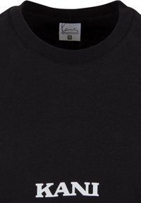 Black cotton t-shirt with a crew neck. Features white "KANi" text across the bottom. Smooth texture, medium weight fabric, size M label.