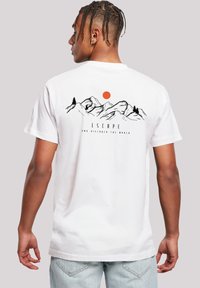 Weißes Baumwoll-T-Shirt mit einem schwarzen Berggrafik, orangefarbener Sonne und dem Text "ENTFLIEHE UND ENTDECKE DIE WELT" auf der Rückseite. Kurze Ärmel.