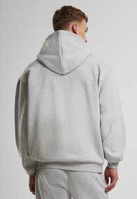 Pelēka kapuce ar brīvu piegriezumu, ribota apkakle un apakša, mīksta auduma tekstūra un plaša kapuce papildu komfortam.