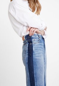 Denim skirt featuring a light blue wash with a dark blue side panel, high waist, and classic five-pocket design. Textured fabric.