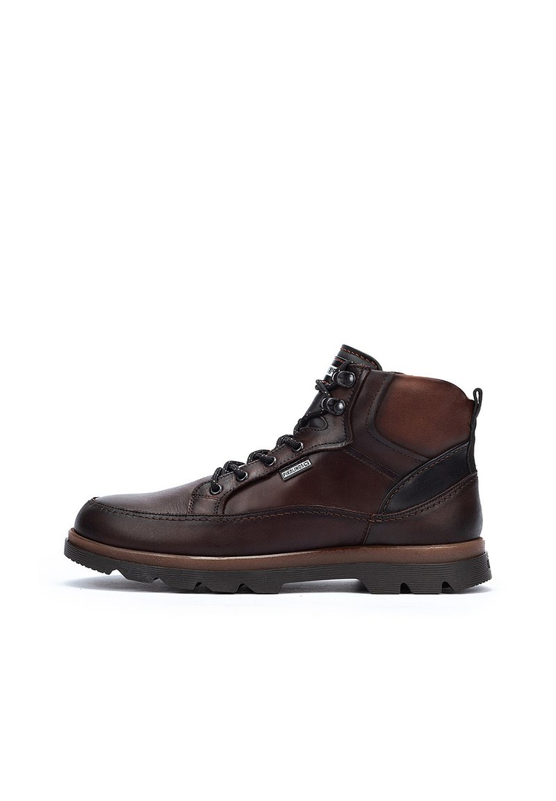 Brown leather boots with a high-top design, black accents, round laces, and rugged soles. Features stitching details and a logo patch.