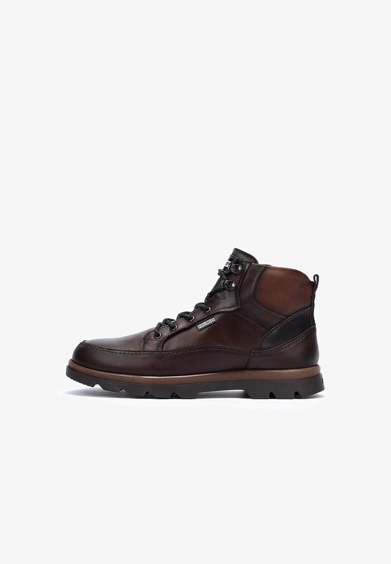 Bruine leren laarzen met een hoge schacht, zwarte accenten, ronde veters en robuuste zolen. Kenmerkt zich door stiksels en een logopatch.