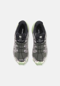 Baskets de sport grises et noires avec une tige texturée, des lacets flexibles et une semelle extérieure en caoutchouc verte avec un motif géométrique.
