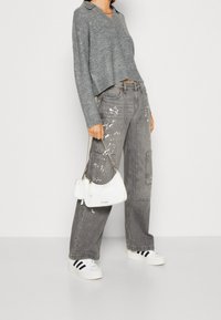 Grå stickad tröja, lösa cargobyxor med färgfläckar, vit axelväska och vita sneakers med svarta ränder. Avslappnad outfit.