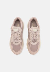 Ljust beige atletiska sneakers med nät- och mockamaterial, en vadderad sula och traditionell snörning. Minimal märkning på tungan.