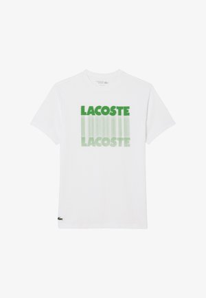 Witte T-shirt met korte mouwen, met groen "LACOSTE"-tekst die twee keer in een verticale vervagingsontwerp op de voorkant is bedrukt, met het Lacoste krokodil logo nabij de zoom.