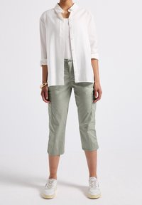 Osoba ubrana w jasne zielone krótkie spodnie cargo, białe trampki, białą koszulkę na ramiączkach oraz rozpiętą białą koszulę z podwiniętymi rękawami.