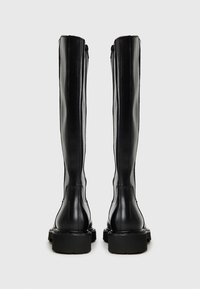 Botas de cuero negras por encima de la rodilla con una textura suave, suela plana y cremallera en la parte trasera. Presentan un diseño elegante y ajustado, con puntera afilada.