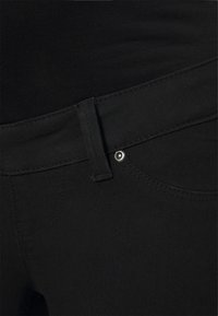 Jeans de mezclilla negros con una textura suave, diseño clásico de cinco bolsillos, herrajes plateados y detalles de costura sutiles.