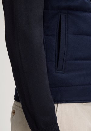 Marineblauer Pullover mit gesteppter Optik und glatten Strickärmeln. Verfügt über eine Seitentasche sowie gerippte Bündchen für Komfort und Passform.