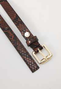 Brown snake print belt with a smooth texture, gold-tone metal buckle, and a decorative metallic logo on the strap.