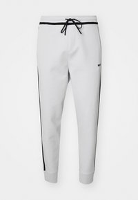 Weiße Sweatpants mit schwarzen Seitenstreifen, elastischem Bund mit Kordelzug, gerippten Knöcheln und kleinem Logo am linken Oberschenkel. Weiche Textur.