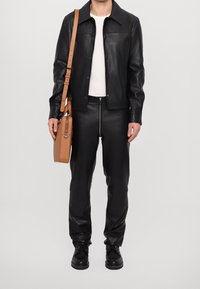 Black leather jacket with a collar, paired with black leather pants and black lace-up boots. Brown crossbody bag with a clasp detail.