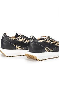 Zapatillas de cuero negro y tejido trenzado con cordones blancos, suela gruesa blanca y acentos beige. Presenta una marca en el talón.