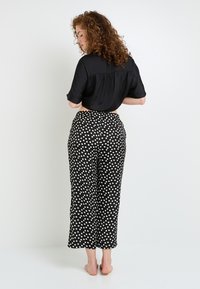 Blouse noire courte avec des manches retroussées, associée à un pantalon noir taille haute à pois blancs. Tissu lisse, coupe décontractée, longueur cheville.