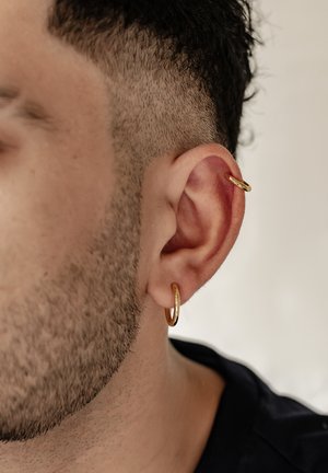 Gold hoop earrings worn in a close-cropped ear, featuring a smooth surface and circular shape. Short hair with a scalp fade.